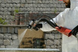 a man in a white coverall spraying water on a brick wall