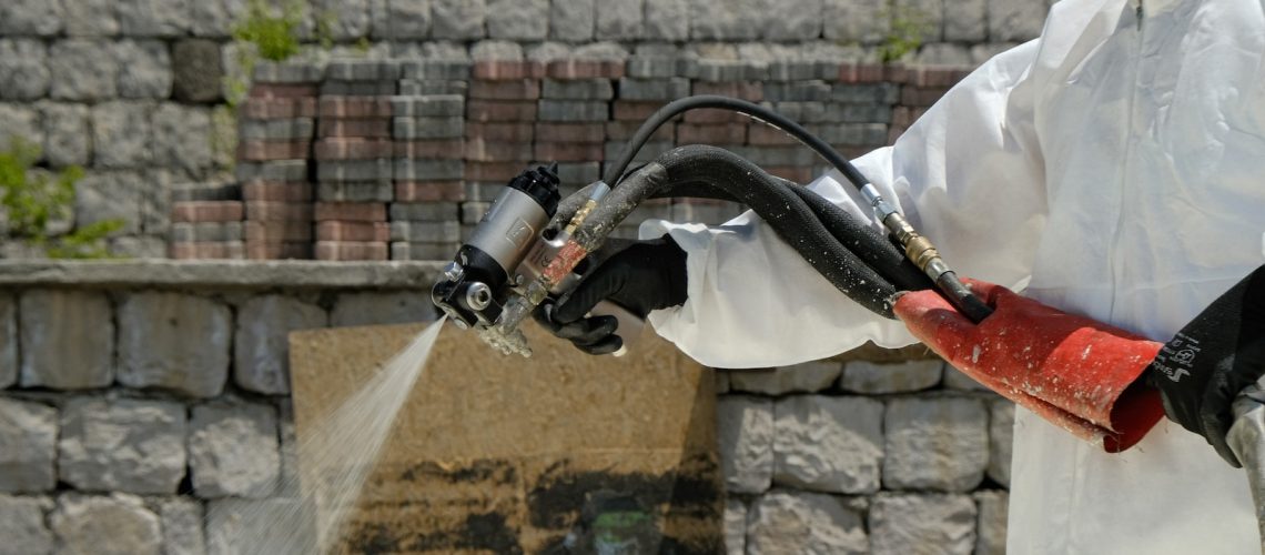 a man in a white coverall spraying water on a brick wall